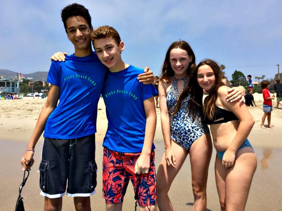 Four teenage campers, two boys and two girls, hanging out together on the beach at Aloha Beach Camp.