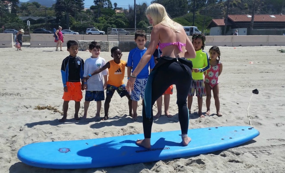 Surf camp director Aurora Eagles giving a surfing lesson on the sand to a group of young Aloha Beach Camp campers.