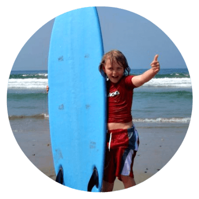 Boy standing on beach holding a surfboard giving 
