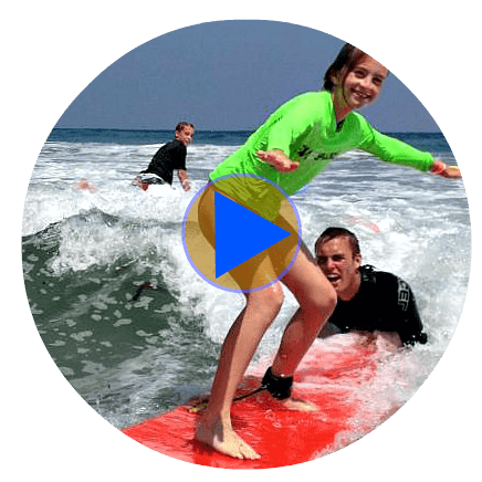Teenage girls surfign with the support and instruction of her surfing instructor Shane McEvoy at Aloha Beach Camp's Los Angeles surf camp. This is a clickable/tapable photo linking to Aloha Beach Camp's Los Angeles surf camp YouTube video page.