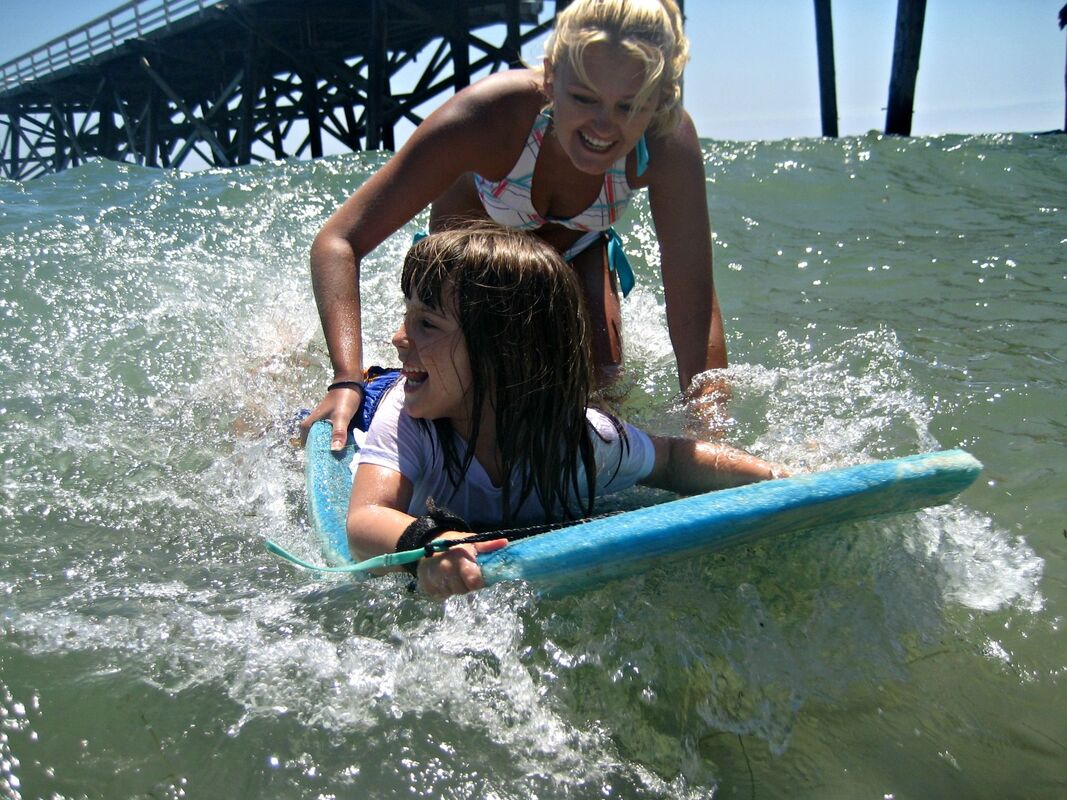 Young happy camper girl receives personalized boogie boarding instruction from her camp counselor at Aloha Beach Camp, one of L.A.'s top beach summer day camps for preschool age kids.