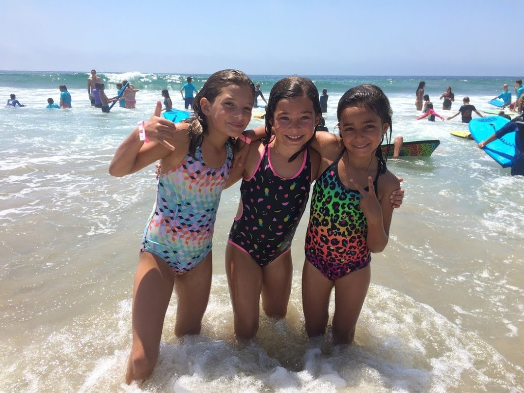 Three girls at Aloha Beach Camp's Kahuna Camp program with arms around each other having fun in the ocean.