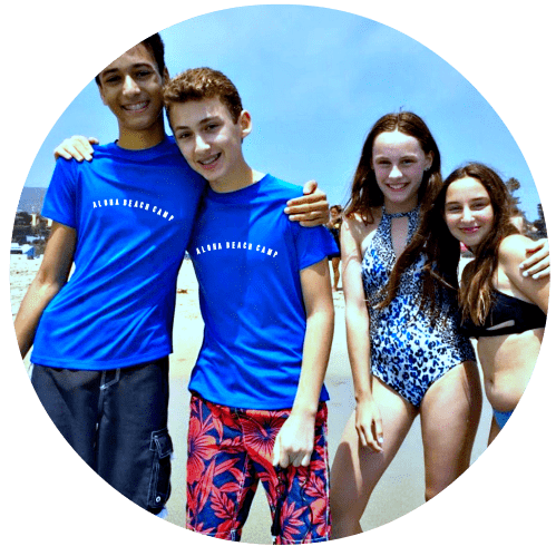 Four teenagers, two boys and two girls, sittign on their towels and hanging out together on the beach at Aloha Beach Camp's High Action summer day camp program in Malibu.