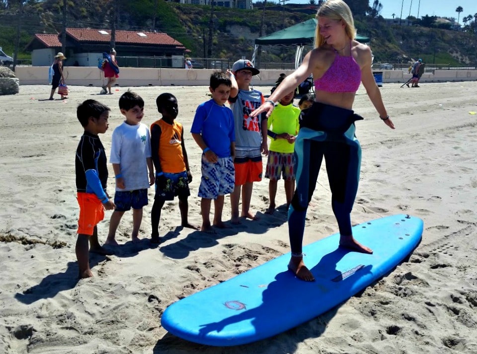 Camp counselor Aurora Eagles gives a surfing lesson to young Aloha Beach Camp kids on the sand at Zuma Beach