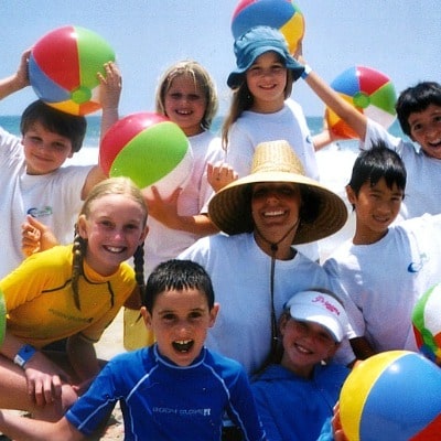 Aloha Beach Camp counselor Melinda Quintero surrounded by a group of happy campers, each holding a colorful beach ball.