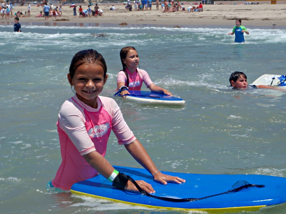 Girls in pink rash guards standing in the ocean with their boogie boards.