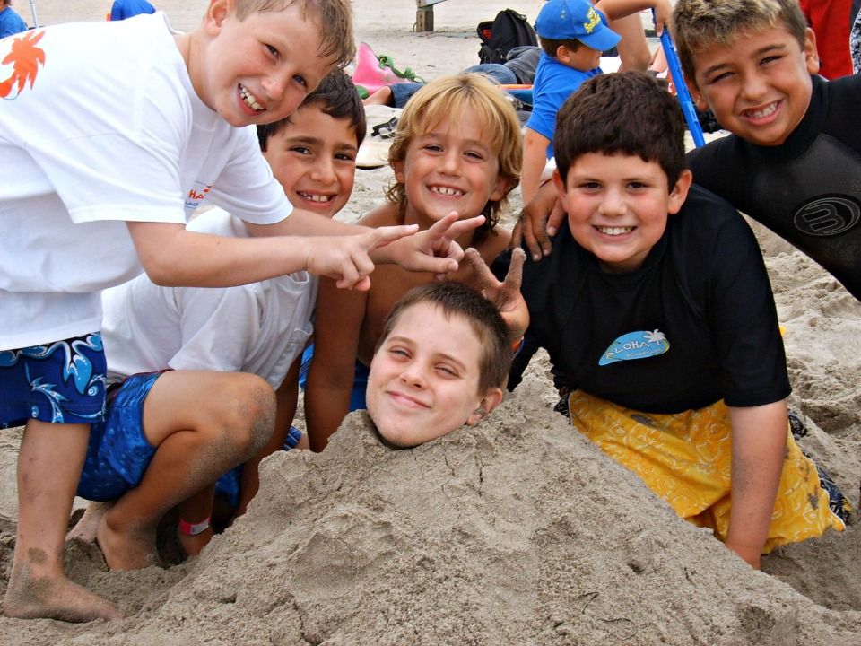 Six boys having fun playing together in the sand at beach summer camp.