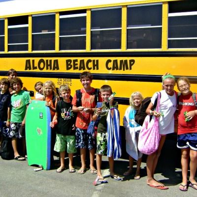 Large group of campers lined up against their Aloha Beach Camp summer camp bus, getting ready to board the bus for the ride home after camp.