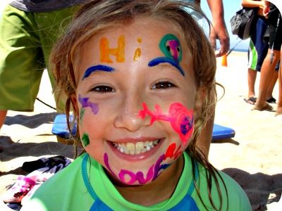 Young girl with colorful facepaint all over her face at Aloha Beach Camp.