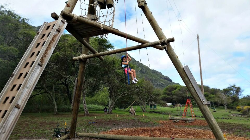Huge picture of a young girl sitting in a swing hanging high above the ground particpating in Aloha Beach Camp's Alpine Tower activity at on Oahu, Hawaii. Aloha Beach Camp's Hawaii summer camp program takes place at Camp Mokuleia on Oahu.
