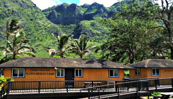 Picture of Aloha Beach Camp's camper sleeping quarters and cabins with beautiful green mountains and palm trees in the background at Aloha Beach Camp's 2021 Hawaii summer Camp program on Oahu.