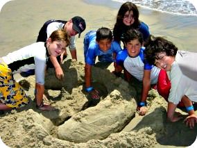 5 boys and a girl sitting and digging a sandcastle together at Aloha Beach Camp