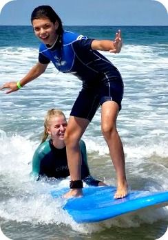 Teenage camper surfing at Aloha Beach Camp with assistance and instruction from her camp counselor.