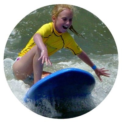 Female camper smiling on her surfboard at Aloha Beach Camp's Malibu surf camp at Zuma Beach.