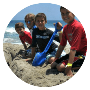 4 boys playing digging holes in the sand, making sandcastles, and playing together on the beach.