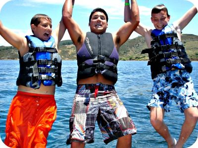Two teenage boys and their camp counselor holding hands while jumping off the back of a boat into Castaic Lake.