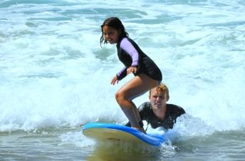 Teenage girl surfing with help of her camp counselor at Aloha Beach Camp Summer Camp in Los Angeles.