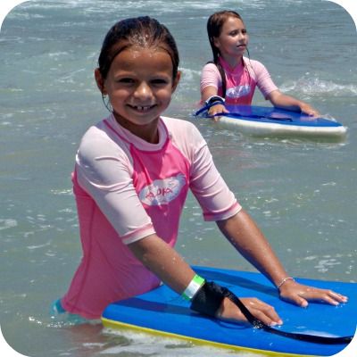 Girl in pink rash guard standing in the ocean and smiling with her hands on her boogie board.