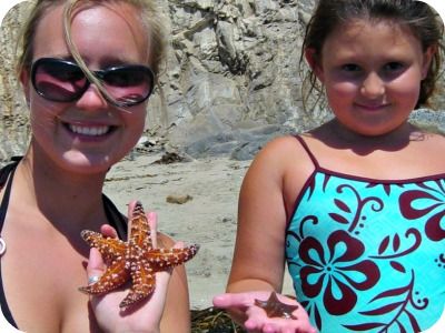 Female camp counselor and young female camper standing on the beach holding live starfish they found at the Paradise Cove tidepools.