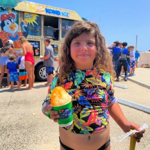 Girl in colorful rash guard holding her shave ice snow cone at Aloha Beach Camp