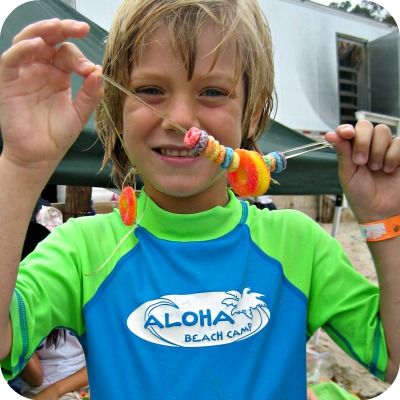 Boy from Sherman Oaks wearing a green and blue Aloha Beach Camp rash guard shows off the Candy Lei he made at camp.