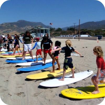Group of 15 Aloha Beach Camp kids from Sherman Oaks standing on their surfboards on the sand, just prior to entering the ocean.
