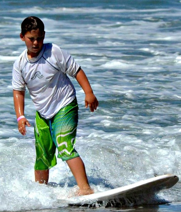 Boy surfing on white surfboard at Aloha Beach Camp's 2017 summer day camp program.