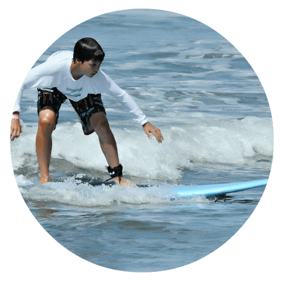 Boy surfing on blue surfboard and wearing a long sleeved white rashgaurd at Aloha Beach Camp's 2018 summer day camp program.