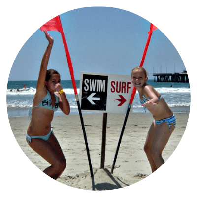 Two girls standing on the beach holding orange lifeguard flags in front of a 