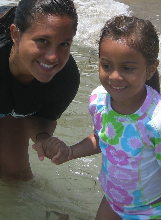 Aloha Beach Camp counselor and young camper holding hands in the ocean.