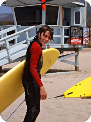 Teenage boy carrying a yellow surfboard at Aloha Beach Camp on Zuma Beach.