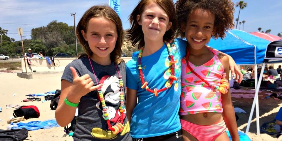 Three campers from Encino hanging out together at Zuma Beach proudly showing off the candy leis they just made at Aloha Beach Camp.