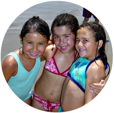 3 young girls at Aloha Beach Camp standing on the beach with arms around each other for the group photo.