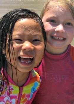 Two young Keiki Camper girls together on the beach laughing, smiling and soaking wet from playing in the ocean at summer camp.
