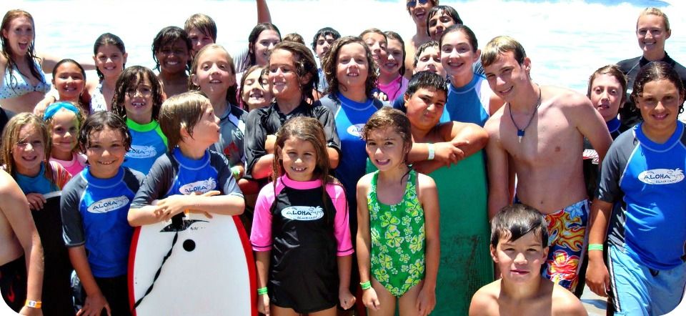 Group of 20 campers standing together on the beach wearing Aloha Beach Camp rash guards.