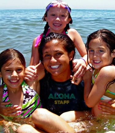 Three young Keiki Camp girls and their Camp Counselor pose for picture in the ocean while attending Aloha Beach Camp's  Paradise Cove, Malibu day camp location.